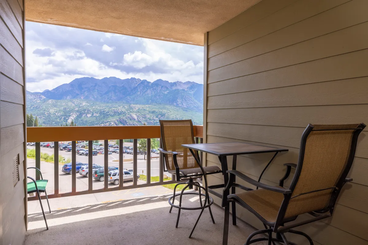 A private balcony is equipped with comfortable chairs and a small table, providing a peaceful spot to enjoy coffee or simply gaze at the mountains. The vantage point highlights the connection between the indoor living area and the breathtaking outdoor scenery.