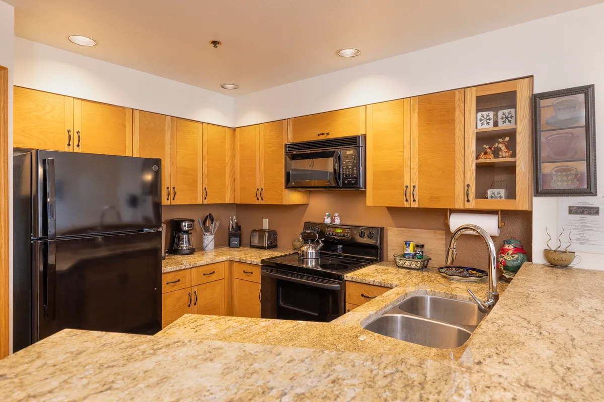 This image centers on a kitchen with a black refrigerator, granite countertop, wood cabinetry, and stainless steel appliances. The setting is designed for cooking and entertaining, with visible elements that suggest both functionality and warmth.
