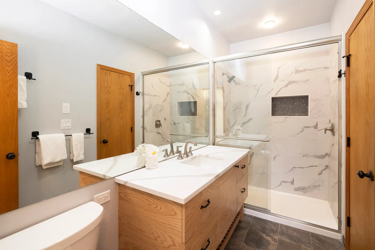 A modern, well-appointed bathroom featuring a double vanity with ample counter space, a glass-enclosed shower, and elegant marble wall tiles. The layout offers both functionality and luxury, creating an inviting space for morning and evening routines.