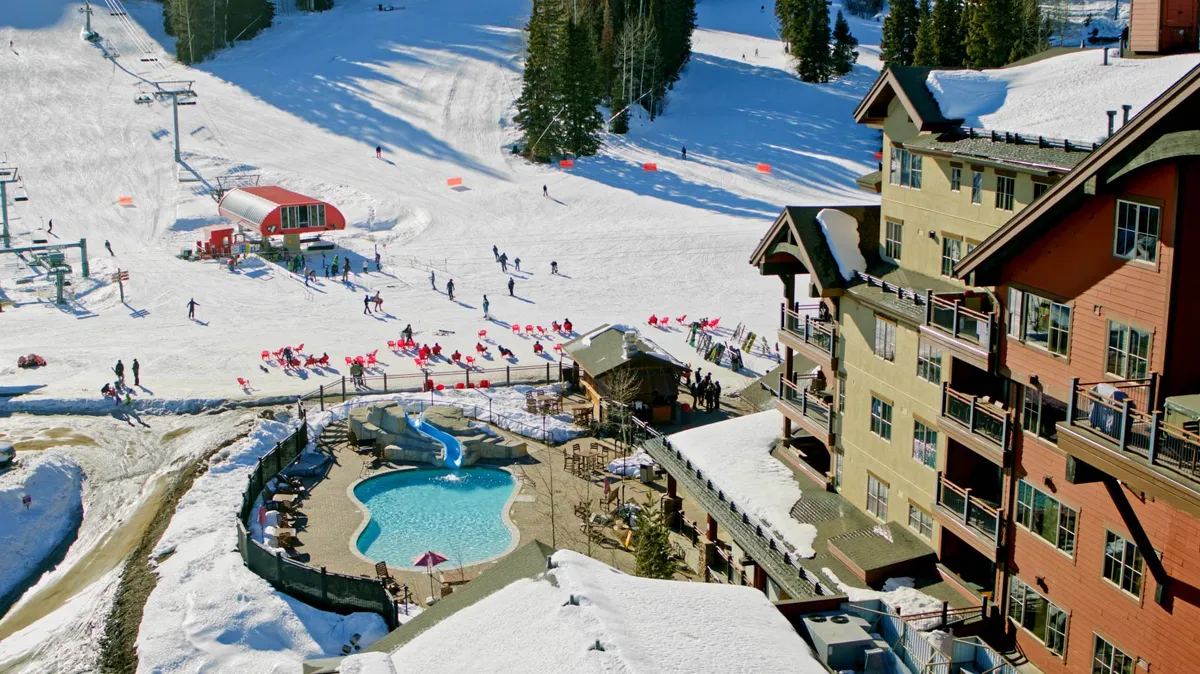 This dynamic exterior image captures the vibrant atmosphere of Purgatory Village, featuring ski slopes, the pool area, skiers in action, a snow-covered landscape, and the resort building all in one frame. The blend of snow sports and relaxation spaces brings together multiple family-friendly activities available right outside the condo.